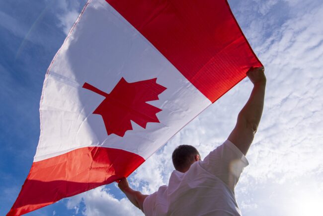 homem-que-mantem-a-bandeira-nacional-do-canada-contra-o-ceu-azul